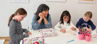 A smiling woman and girls at a table working on WipalaBox learning activities.