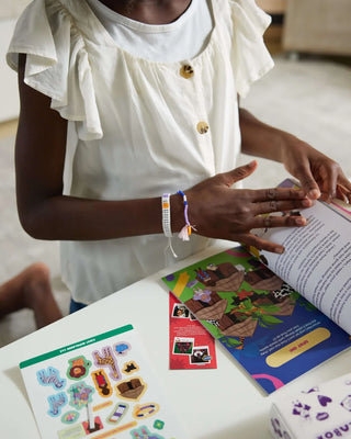 Girl doing an activity from the Maasai Adventure illustrated book by wipalaBox using stickers and educational materials.