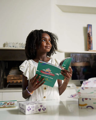 Young girl holding and reading the Maasai Adventure activity book by WipalaBox, an educational and cultural learning kit for kids at home.
